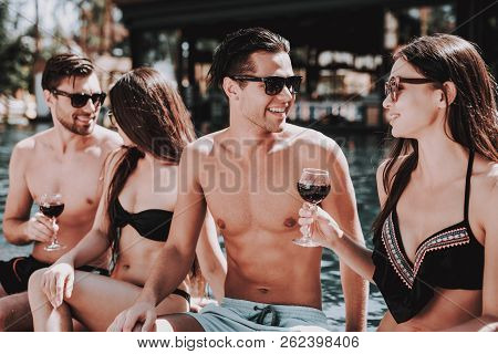Young Smiling Friends Drinking Wine At Poolside. Group Of Young Happy People Sitting At Poolside Tog