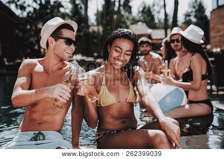 Smiling Couple With Alcoholic Drinks At Poolside. Beautiful Black Woman And Young Man Holding Bottle