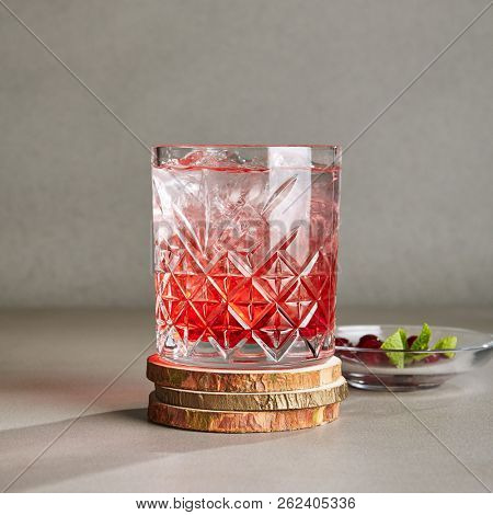 Cold Clear Drink of Red Berries with Ice, Water, Sugar in a Crystal Glass on Wooden Plate. Refreshment Cranberry Iced Tea, Beverage, Cocktail, Punch, Lemonade, Fruit Drink or Compote Close Up