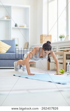 Fit brunette girl doing push-ups on mat while exercising in living-room at home