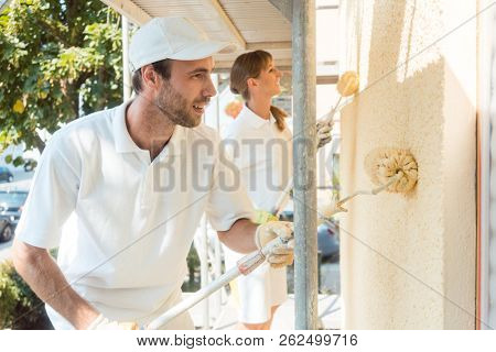 Painter and colleague painting wall with roller, side view
