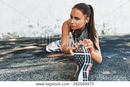 Horizontal Image Of Fitness Young Woman Streching And Listening The Music On Earphones Before Outdoo