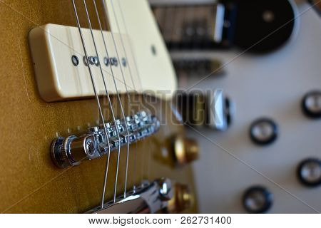 Gold top and white electric guitars closeup with P90 pickup. Body, pickups, bridge, strings, pickguard and knobs.
