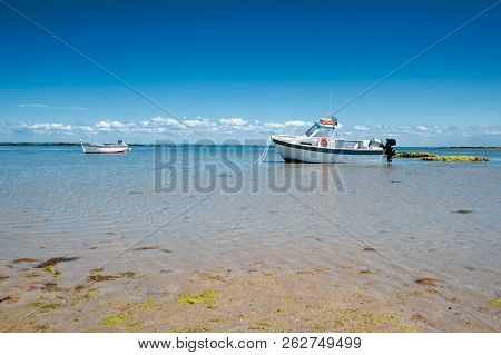 Boat Resting On Sand At Lowtide In Summertime Surround With Clear Water