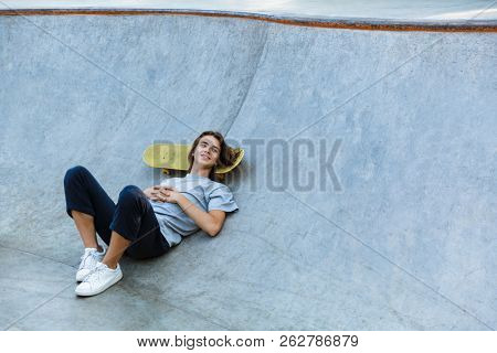 Cheerful young teenge boy spending time at the skate park, laying on a skateboard at a ramp