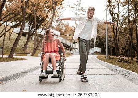 Excited Man Riding Skateboard And Disabled Girlfriend Smiling To Him