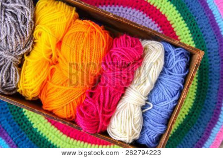Knitted Striped Mat And Colorful Skeins Of Wollen Yarn On Wooden Background.