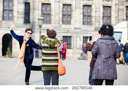 Amsterdam, Netherlands- March, 2018: Asian Tourists Using Their Cellphones To Take Pictures At Dam S