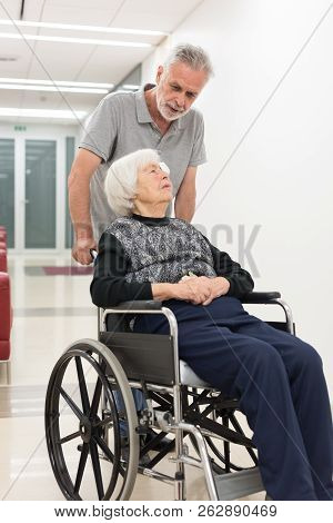 Middle Aged Man Helping And Taking To Elderly 95 Years Old Woman Sitting In The Wheelchair.