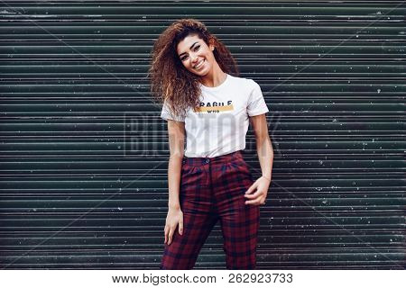 Smiling Young Arabic Woman With Black Curly Hairstyle. Arab Girl In Casual Clothes In The Street. Ha