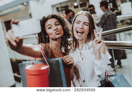 Two Girls With Packages Taking Selfie In Mall. Using Smartphone. Digital Device In Hand. Shopping Co