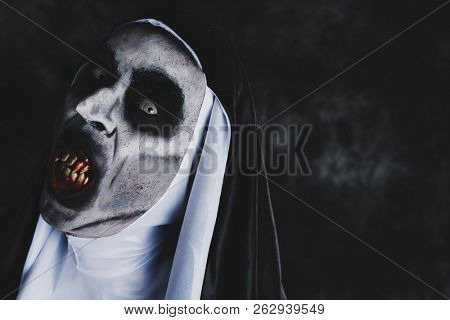 closeup of a frightening evil nun, with bloody teeth and scary eyes, wearing a typical black and white habit, against a dark background, with some blank space on the right