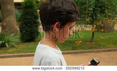Young Teenager With Smartphone Walking In City, Slow Motion . The Boy Walks On The Street And Looks 