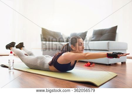 Young Woman Doing Sport Workout In Room During Quarantine. Lying On Mat And Stratching Forward With 
