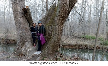 Two Women In Coats And Sneakers Posing By Tree In The Forest By Trail N Orange County, North Carolin