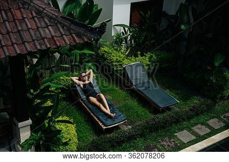 Young Woman Relaxing On A Deck Chair In Courtyard Of A Tropical Resort House