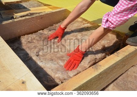 Constructing A Rooftop A Building Contractor In Protective Gloves Is Lying Glass Wool Batt Insulatio