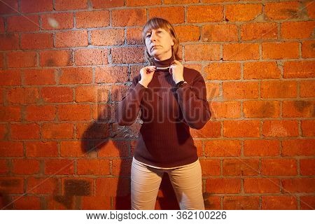 A Middle-aged Woman Poses Showing Clothes Near Red Brick Wall. An Inept Model In An Inept Shoot