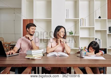 Happy Mixed-race Parents Looking At Their Daughter Drawing Picture With Pencil