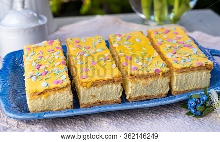 Four Tompouce Cakes With Whipped Cream And Yellow Icing Served In Sunny Spring Garden