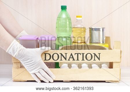 Food Box, Donation, Volunteers Help Those In Need Of Food. Hands In Gloves Hold Out A Wooden Box Wit