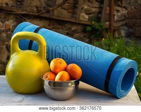 Karemat, Kettlebell And Tangerines On A Wooden Table Outdoors