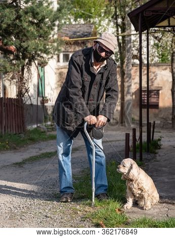 Senior Man In Protective Mask With A Cane Walking With A Dog In Sunny Day