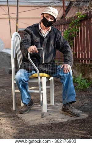 Senior Man In Protective Mask With A Cane Sitting On A Chair