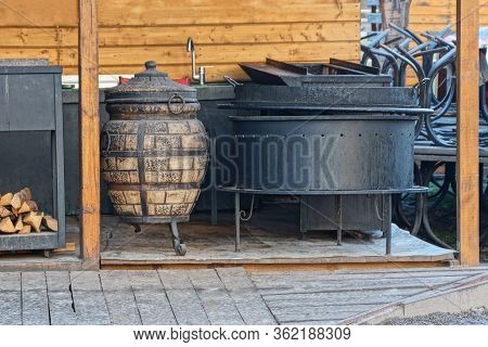 A Black Iron Cauldron And A Wooden Barrel Stand Outside Against A Brown Wall
