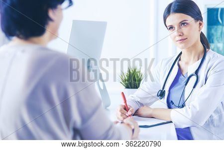 Doctor and patient discussing medical problems in a hospital consulting room. Doc filling in a patient's form