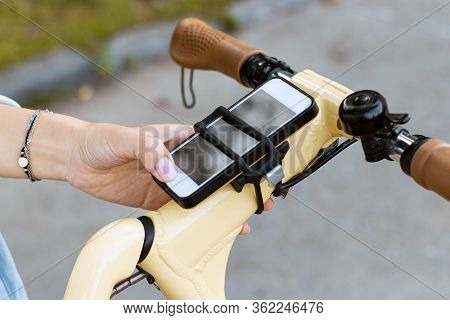 Woman Hand Uses The Phone. The Smartphone Is Attached To The Bicycle Steering Wheel
