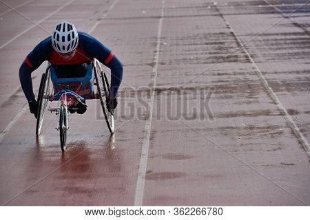 Preparing for wheelchair marathon. Paraplegic male athlete in racing wheelchair warming up alone at outdoor track and field stadium