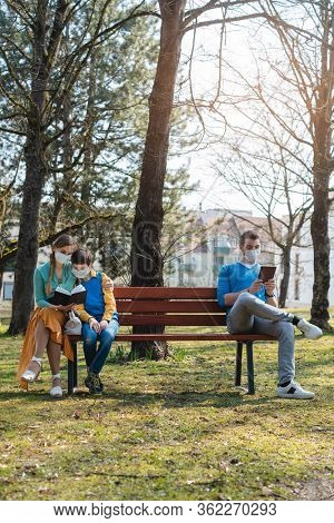 People sitting on park bench in the sun practicing social distancing in corona crisis wearing masks