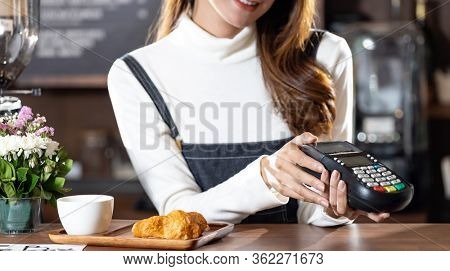 Asian Barista woman holding creadit card reader machine cashless payment for coffee purchase at cafe. Cashless preventing from coronavirus covid-19 Spreading and infection, Panoramic web banner crop.