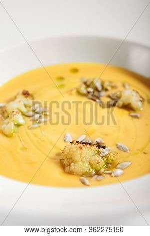 Pumpkin soup in white bowl. Served main course close up. Vegetable cream soup decorated with seeds. Restaurant food portion, main course. Vegetarian supper. Dinner, gourmet meal in plate