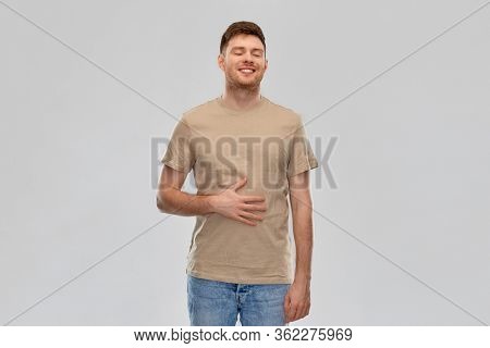 digestion, satisfaction and people concept - happy smiling full man touching his tummy over gray background