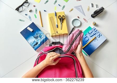 education and learning concept - hands packing pink backpack with pencil-case, books and school supplies on table