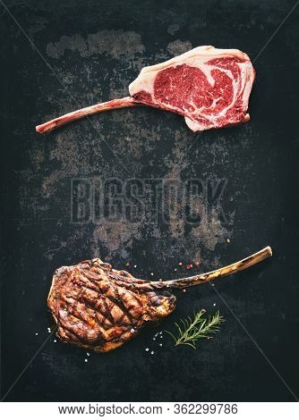 Black angus Tomahawk beef steaks raw and grilled with seasoning on dark rustic background
