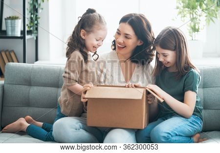 Mother and daughters are unpacking cardboard box at home.   