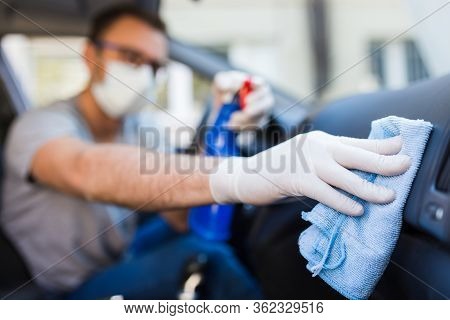 Driver With Face Surgical Mask Using Disinfectant And Microfiber Cloth To Clean Car Interior.