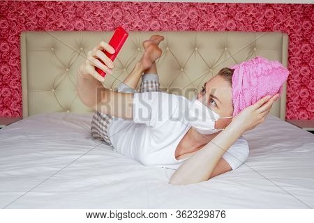 Home Quarantine. A Young Caucasian Blogger Girl In A Protective Medical Mask And A Towel On Her Head