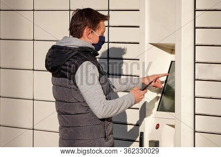 A Young Man In A Blue Mask Picks Up A Package At Boxes For Parcels. Contactless Or Non-contact Deliv