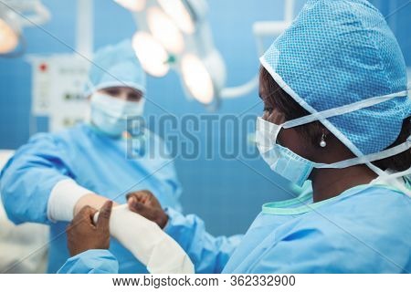 Female surgeon helping her co-worker in wearing surgical gloves at operation theater