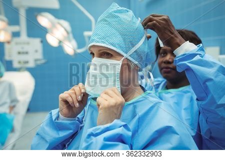 Female surgeon helping her co-worker in wearing surgical mask at operation theater