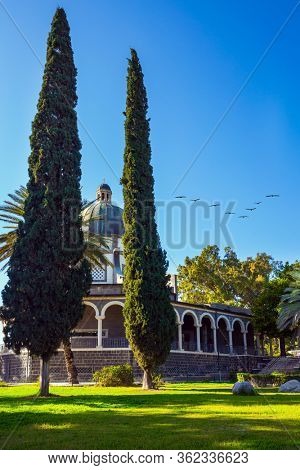  The Catholic Church of the Italian female Franciscan monastery on Mount Bliss in the Galilee. Flock of migratory birds flies. High shore of Lake Tiberias. The concept of religious pilgrimage tourism