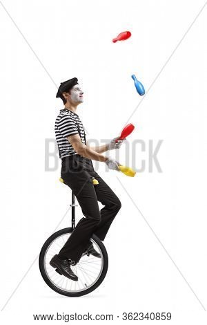 Full length profile shot of a pantomime guy riding a mono-cycle and juggling isolated on white background