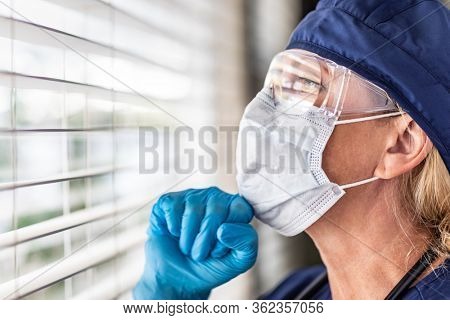 Female Doctor or Nurse On Break At Window Wearing Medical Face Mask and Goggles.