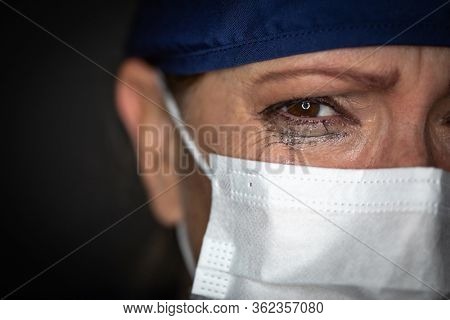 Tearful Stressed Female Doctor or Nurse Wearing Medical Face Mask on Dark Background.