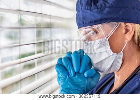 Stressed Female Doctor or Nurse On Break At Window Wearing Medical Face Mask and Goggles.