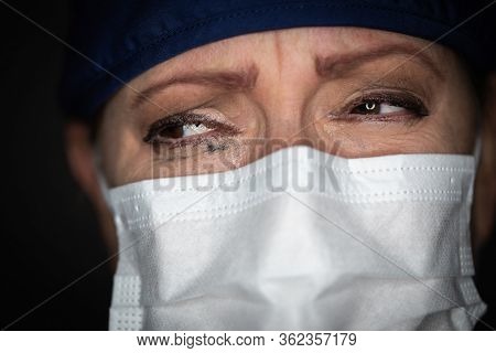Tearful Stressed Female Doctor or Nurse Wearing Medical Face Mask on Dark Background.